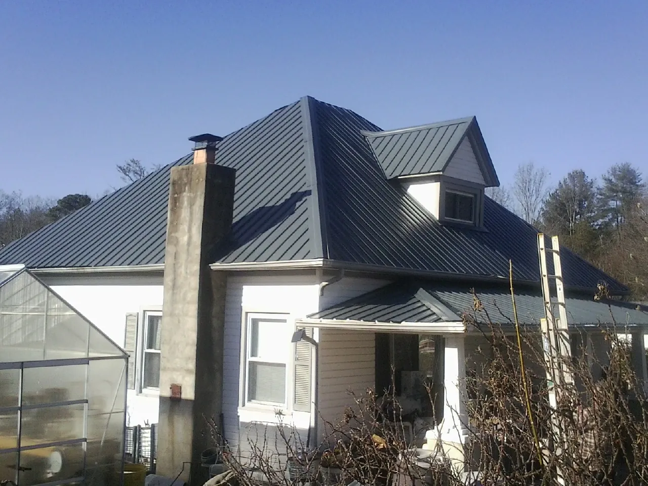Dark blue standing seam metal roof on a white farmhouse with dormer — Slate & Tile Roof Repair by Roofing Brothers in Conroe