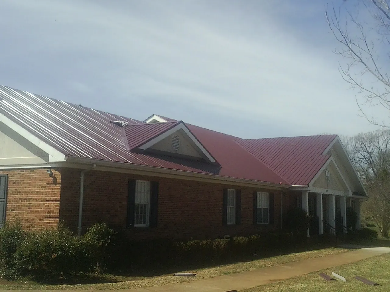 Red metal roof with gabled entries on a long brick building, from a Hail Damage Roof Repair job in Conroe