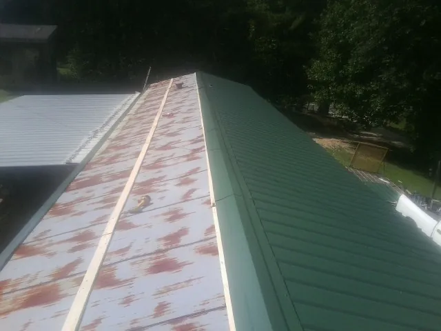 Old rusted panels beside newly installed green metal roofing — Wind Damage Roof Repair by Roofing Brothers in Conroe