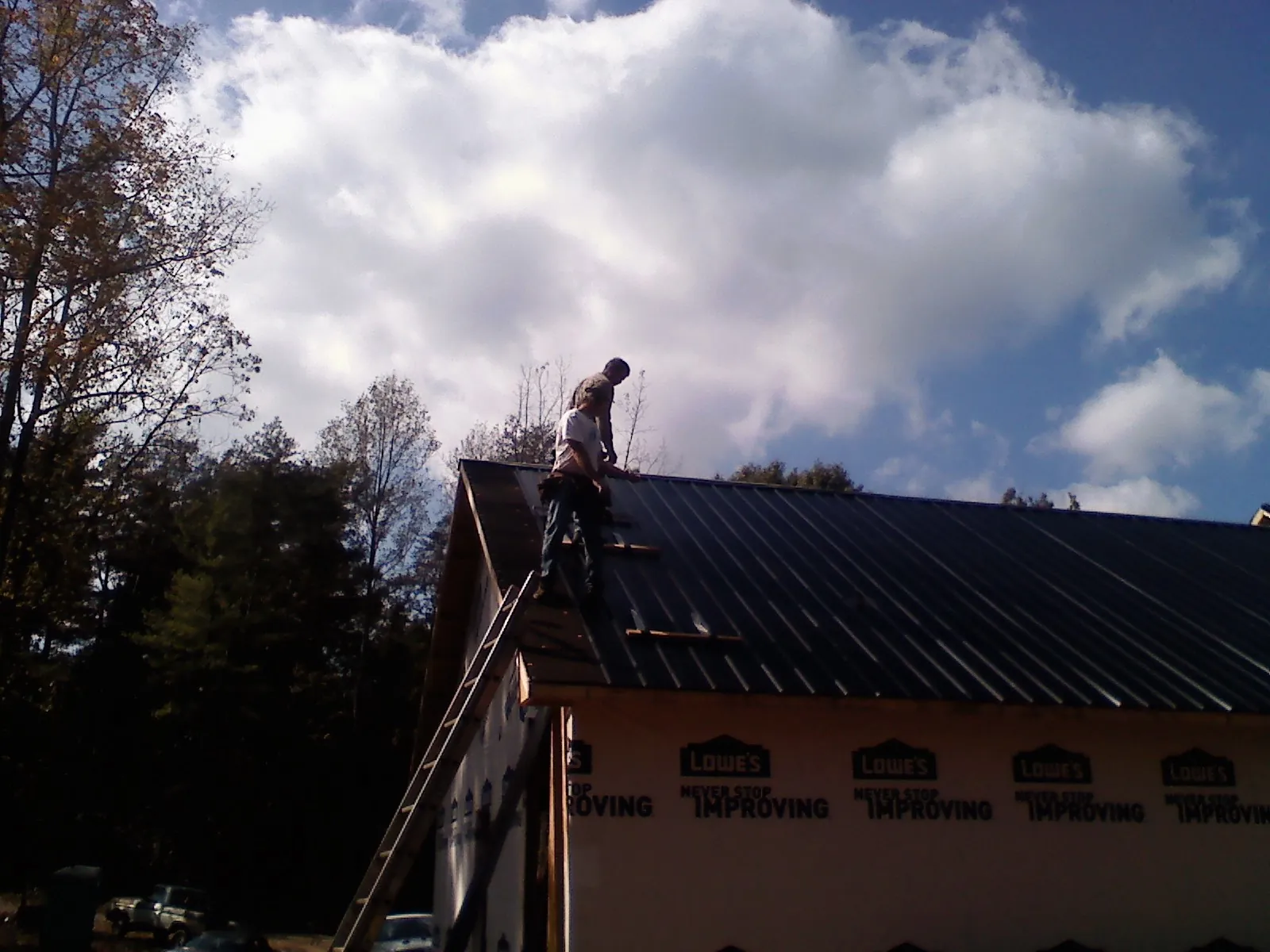 Roofer fastening dark metal panels high against a cloudy sky, from a Roof Inspection job in Conroe